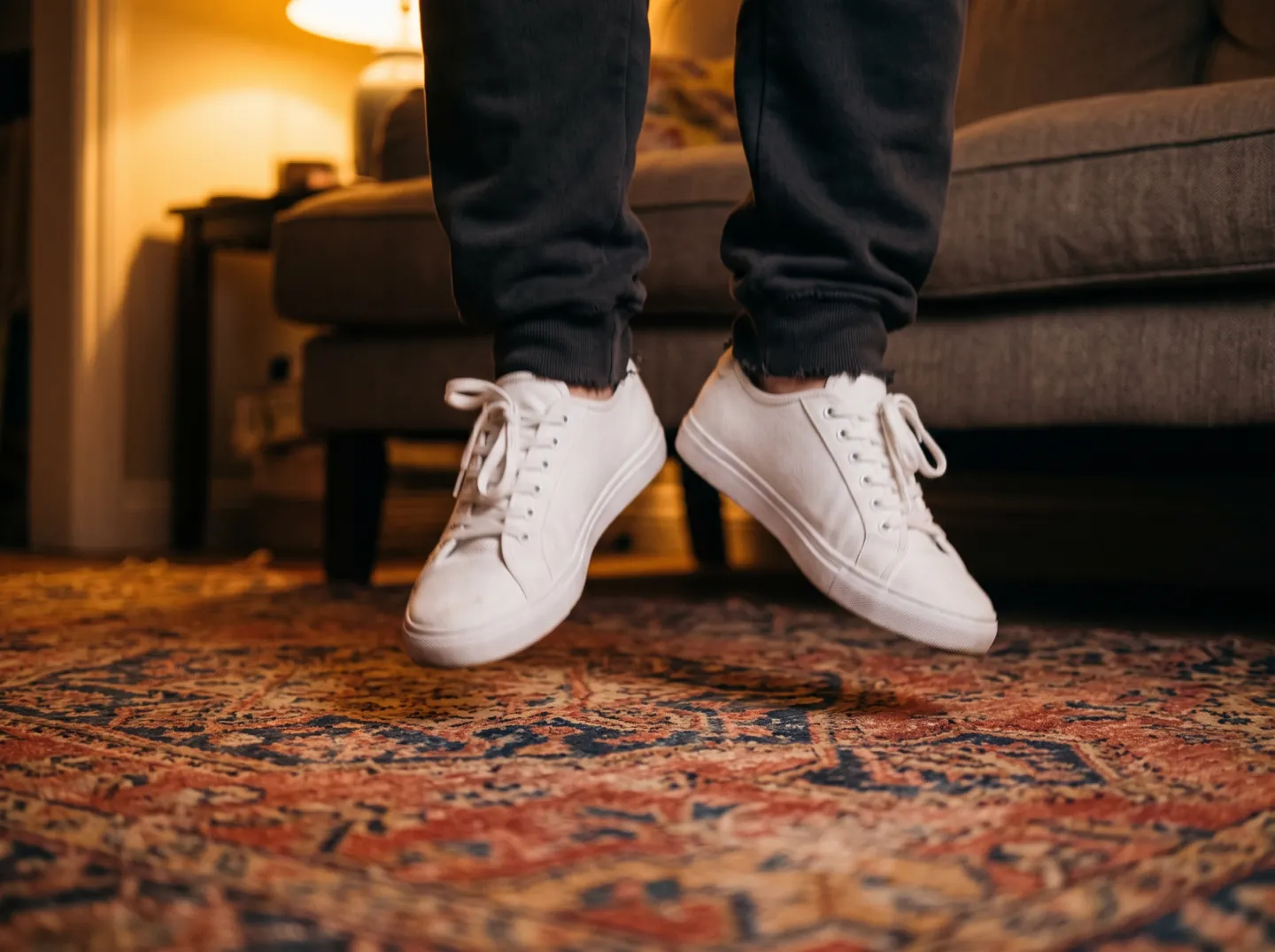 Feet in trainers caught mid-jump above a patterned living-room rug